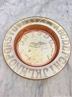Top view showing raised alphabet letters and numbers around the rim and bird design in center