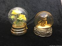 Two musical glass globes: one with yellow dry flowers in a gold base, one with gold angel snow globe in silver ornate base