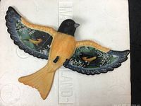 Front view of the Oriole bird ornament showing the black head, orange body and detailed wings with painted Oriole scenes.