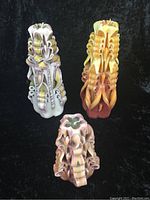 Three multicoloured vintage sculpted candles showing intricate curled designs in purple, green, yellow/orange and brown tones on black background.