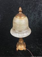 Vintage glass lamp with bronze base shown unlit on a black background.