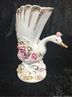 Front angled view of ceramic swan vase with visible gold accents on beak and decorative base. Pink roses and scalloped top opening shown.