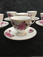 Close-up of one teacup on matching saucer showing pink rose design and gold trim detail on white porcelain.