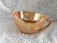 Full side view of the glossy peach luster finish Fire King mixing bowl with handle and pouring spout.