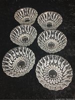 Top-down view of six glass dessert bowls arranged in two columns of three on a black surface showing shape and pattern.