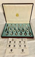 Set of 12 Canadian Centennial teaspoons displayed in original wooden box with fabric lining, including informational cards describing each crest.