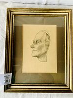 Framed charcoal sketch showing a man's profile signed and dated 1912 by E. Camies. The wood frame is gold-toned with clear glass protection. The sketch is centrally mounted on cream paper with a mat board in the frame.