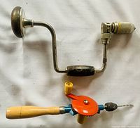 Hand drills shown with wooden handles, metal cranks and gear mechanisms, one drill with orange gear and small drill bit visible