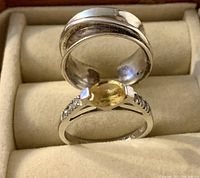 Two sterling silver rings displayed in a beige ring holder; one with an oval amber gemstone and clear crystals, the other a wide plain band with a twisted design.