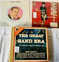 Three vintage vinyl record albums laid flat: Glenn Miller Superselections with pink portrait, Glenn Miller Tuxedo Junction album with tuxedo figure, The Great Band Era compilation with blue, orange, and white cover