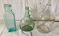 Three vintage glass jugs displayed against a white backdrop, showing their colors and shapes.
