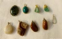 Nine assorted gemstone pendants and charms arranged on a white background, showing size and variety