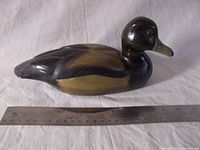 Side view of a hand carved and painted wood duck figurine with ruler for size reference