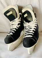 Pair of black CCM Champion 90 ice hockey skates size 8 showing front and side angles with white laces and blade holders on carpet floor.