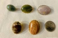 Five handcrafted gemstone brooches or pins laid flat near a quarter for size comparison. Various gemstone colors and patterns visible.