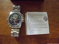 Steel wristwatch with black dial and tachymeter bezel alongside an instruction sheet detailing functions and charging info.