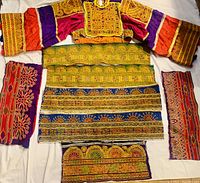 Front view of colorful embroidered long-sleeve costume top with separate embroidered panels arranged on white surface.