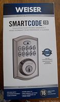 Front of the retail box showing Weiser SmartCode 10 electronic deadbolt lock in satin nickel with 10-digit keypad and key cylinder.