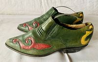 Side view of green leather shoe with red and yellow leather decorative appliques and slight heel.