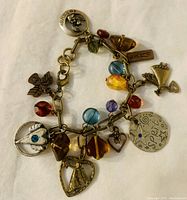 Charm bracelet laid flat showing copper chain with various colorful glass prisms and multiple charms including angels, hearts, fans, and a circular 'Spirit' charm.