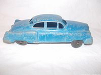 Side view of blue vintage toy car showing worn paint and steel frame with rubber tires.