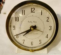 Front view of vintage Baby Ben Westclox wind-up alarm clock showing the clock face with black Arabic numerals, black hour and minute hands, and the brand name on the dial.
