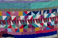 Front view of the multicolored patchwork quilt showing varied fabric pieces in squares and triangles arranged in rows, with visible white tie knots.