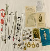 Top-down view showing the full assortment of religious items including necklaces, rings, medallions, rosaries, prayer cards, and booklet on white background