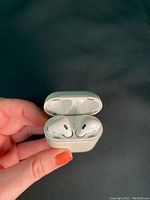 AirPods in charging case held in hand showing earbuds and case, visible dirt and scuffs inside the case