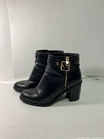 Pair of black ankle boots showing side profile with gold buckle and zipper detail.