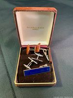 Open box showing all cuff links and tie pins inside. Velvet and satin lined box with brand name inside lid.