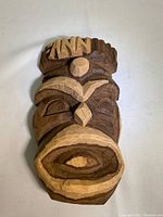 Front angled view of the wooden tiki mask showing carved facial details and wood grain.