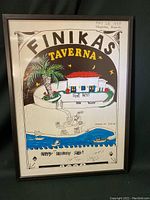 Framed hand printed poster of Finikas Taverna showing overall front view with building, palm tree, stars, moon, and water scene.