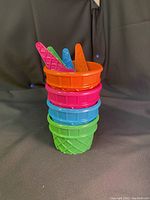 Stacked view of four colorful ice cream bowls with matching spoons inside, showing their waffle cone textured design and vibrant colors.