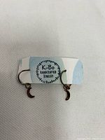 Front view of earrings showing crescent moon pendants on small hoops with K-Bo label behind them.