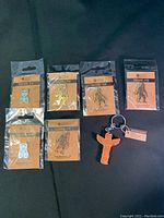 Photo showing all 6 enamel pins individually packaged and 1 totem key chain together on black fabric background.