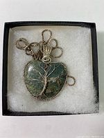 Close-up image showing the heart-shaped semi-precious stone pendant with wire wrapped tree design and chain coiled inside a box with white padding.