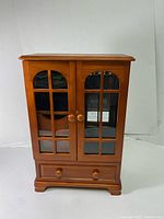 Front view of medium brown wooden jewelry box with two glass-paneled doors and two round knobs, three drawers at the base.