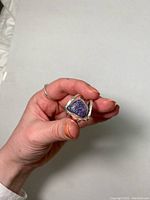 Close-up of hand holding sterling silver ring showing triangular semi-precious purple-blue stone with textured surface and polished silver setting.