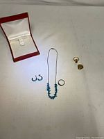 Photo showing the entire jewelry set arranged on light surface including earrings, necklace, two rings, heart locket, and an empty red jewelry case.