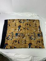 Folded scarf showing Egyptian-themed printed fabric with black border on a white background.
