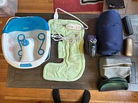 Full view of all items on table showing foot bath, heated shoulder pad, shaver, travel pillow, organizer and eyeglass cases.