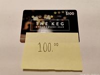 Front of The Keg Steakhouse + Bar gift card showing $100 value in top right corner with blurred lights background.