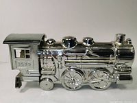 Side view of silver train locomotive showing detailed wheels, cab with windows and smokestack.