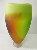 Front view of the green, orange, and brown gradient glass vase on a frosted base