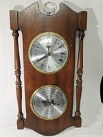 Full view of the wooden framed clock and barometer. Two silver circular dials with brass edges, mounted vertically.
