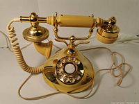 Full view of the French-style rotary dial telephone, showing the brass/gold-tone finish, handset, and coiled cord.
