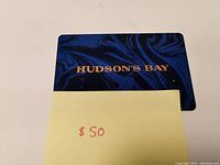 Photo shows a blue and black marbled design Hudson's Bay gift card with a sticky note indicating $50.