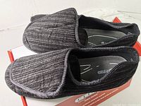 Side view of that shows black textured ribbed fabric slippers with closed toes and cushioned insoles.
