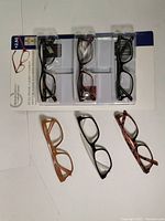Top view of all six pairs of reading glasses, three new in package on top and three used below.